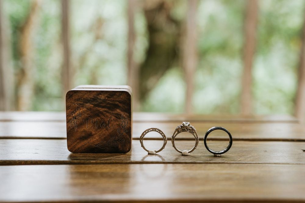Wedding rings and jewelry artistically arranged on wooden surface with soft natural lighting.