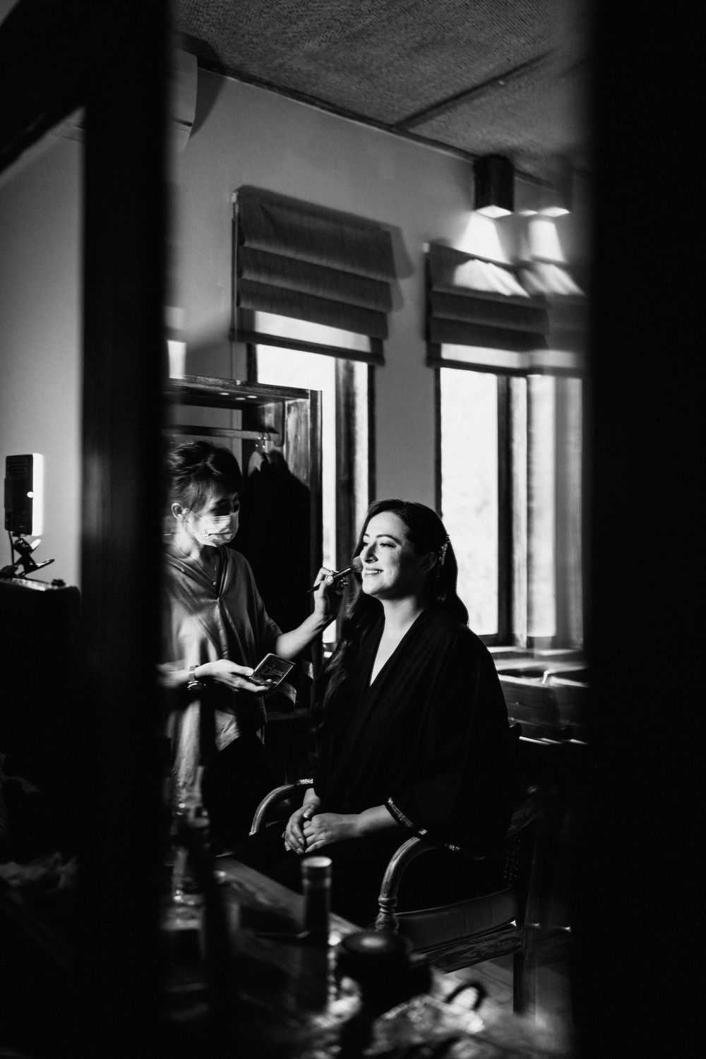 Dramatic black and white photo of wedding preparation in a room with natural window light.