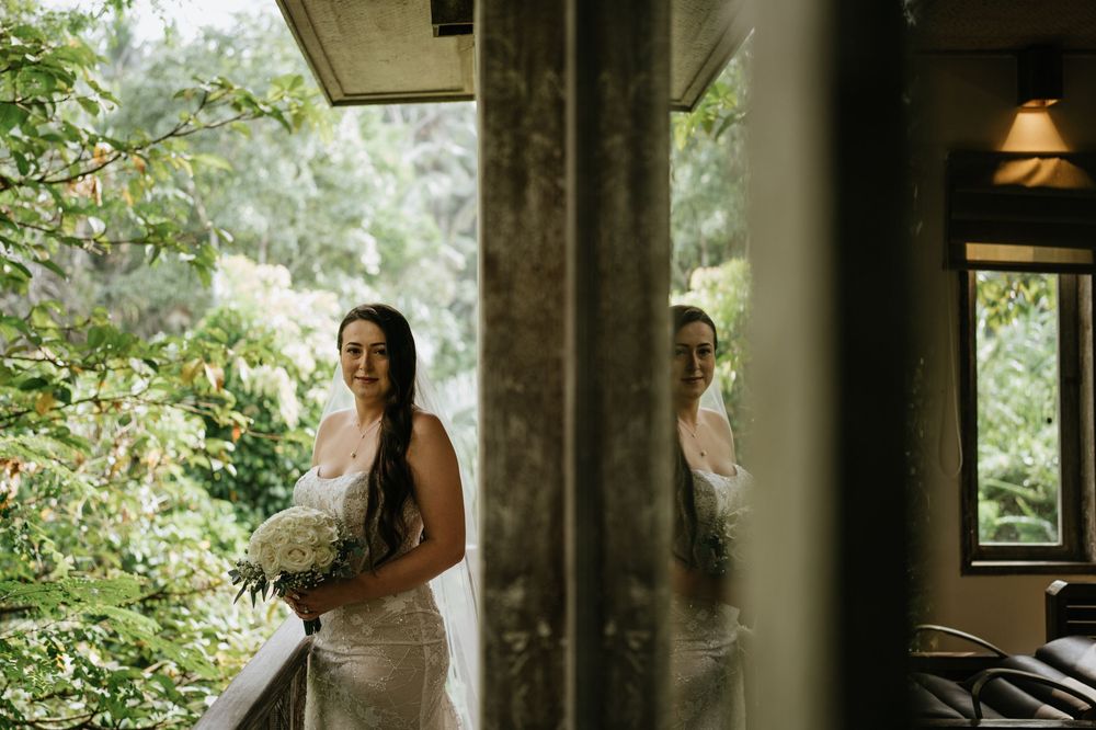 A wedding couple walks through a lush garden pathway with stone walls and tropical plants.