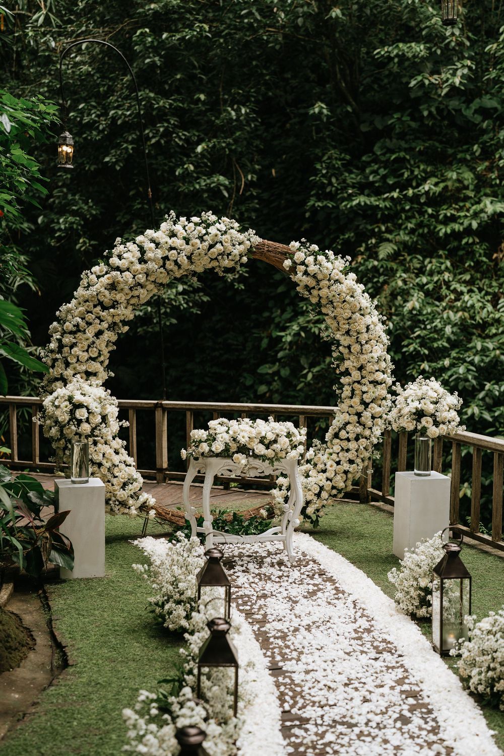 White floral wedding arch with scattered petals creates a romantic garden ceremony setting.