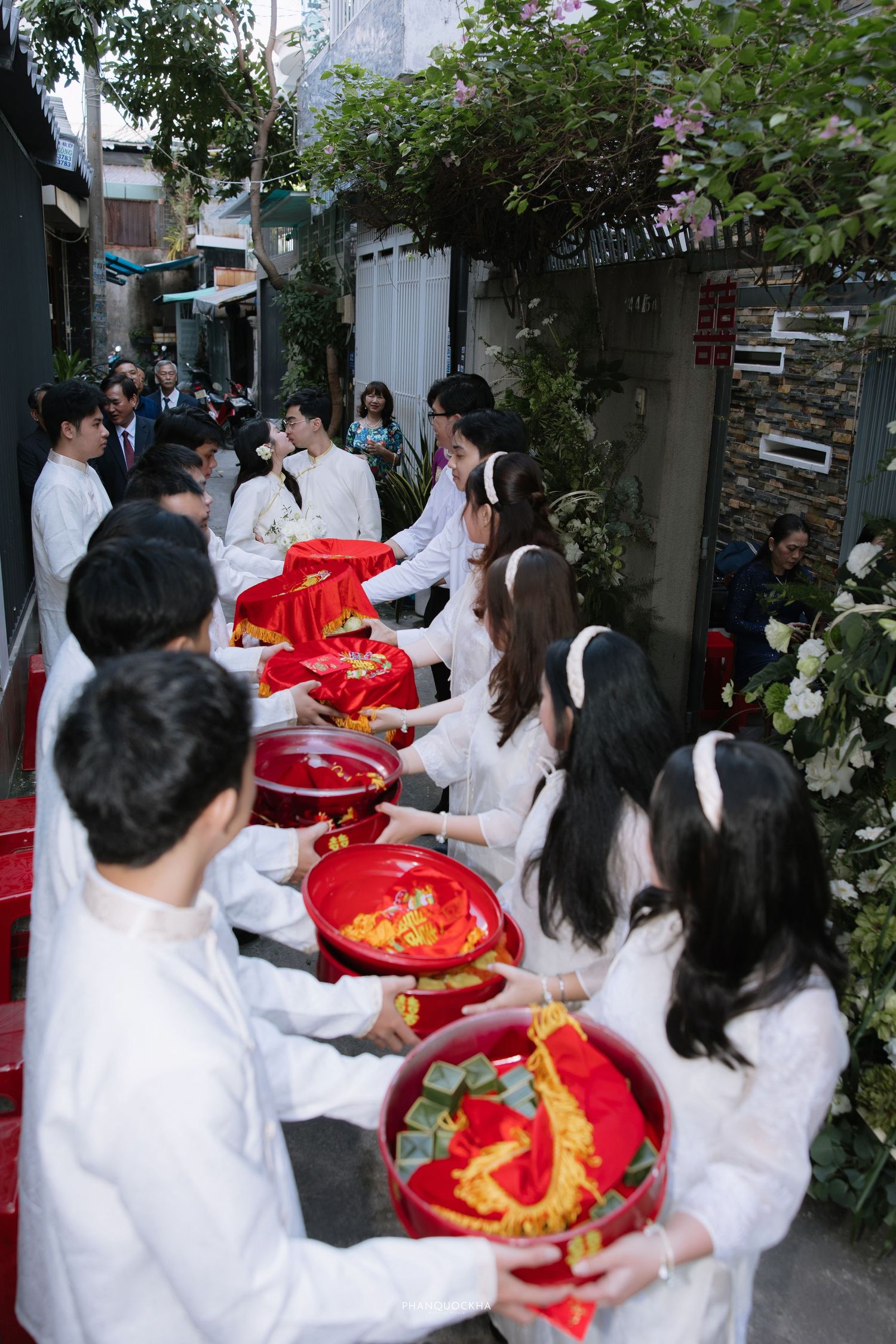 Traditional Vietnamese wedding gift procession with attendants carrying red trays in a narrow alley.