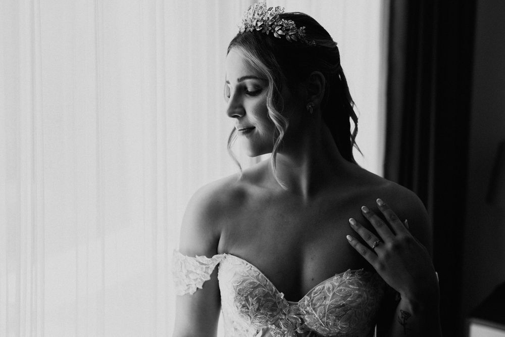 Soft window light illuminates a bride in an elegant white dress.