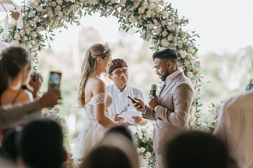 Wedding ceremony under a floral arch with white and blush flowers.