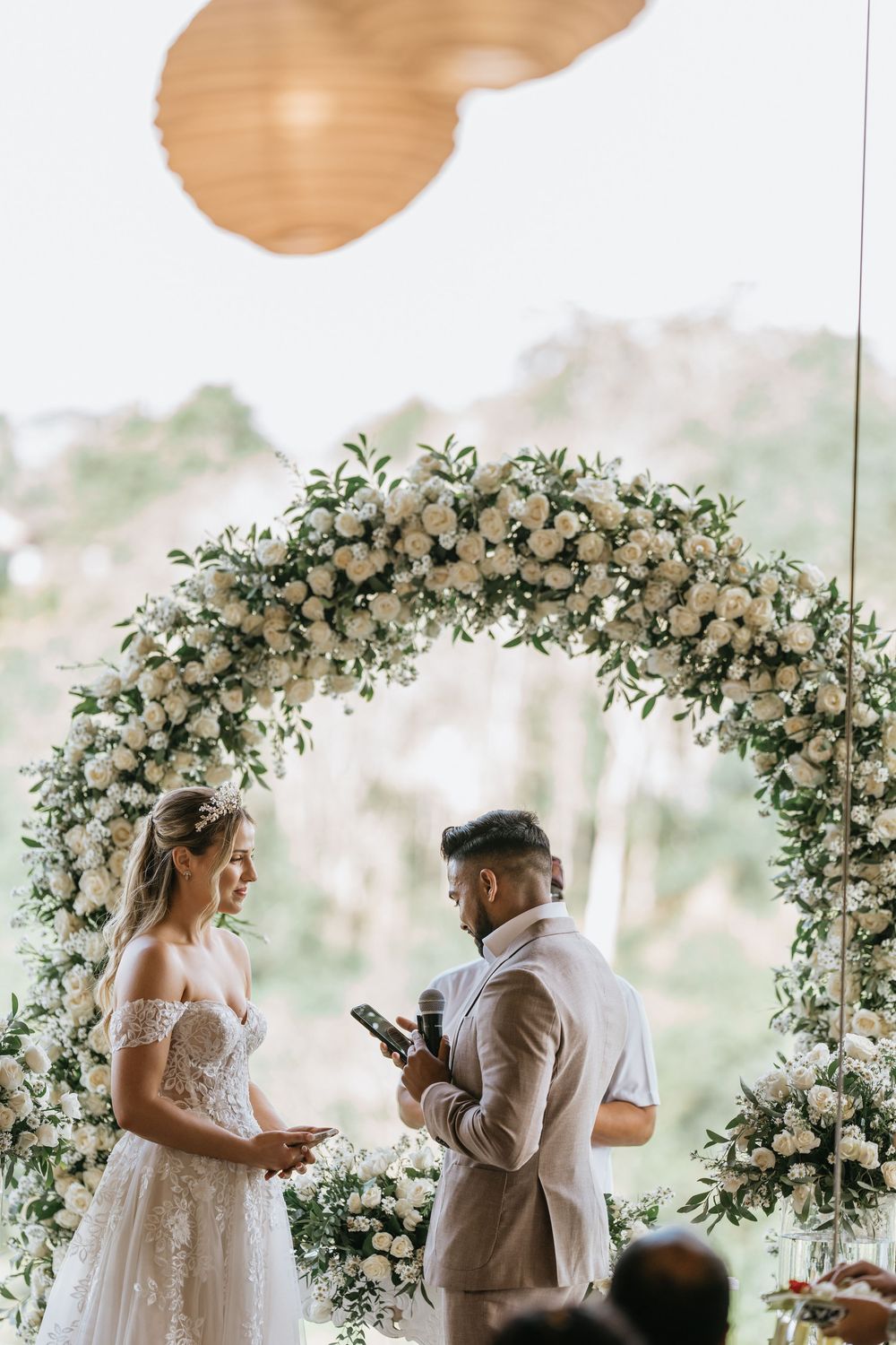 A wedding ceremony under a stunning floral arch with white roses and greenery in an outdoor garden setting.