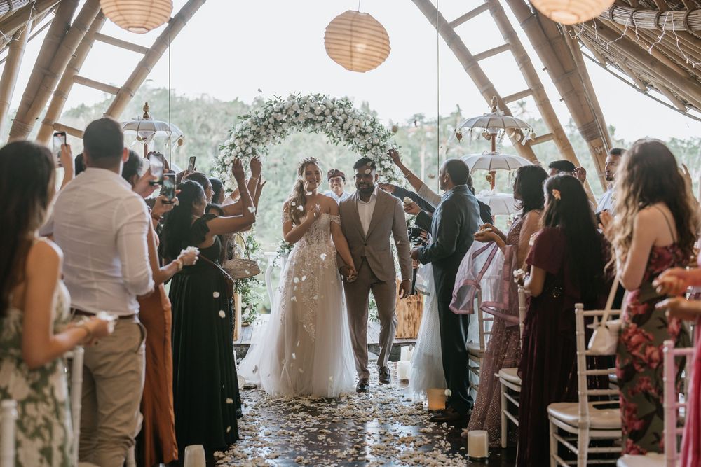 Wedding ceremony in a glass-roofed venue with floral arch and guests celebrating the newlyweds.