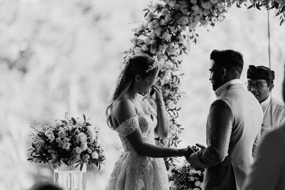 Black and white photo of wedding ceremony under floral arch with emotional exchange.