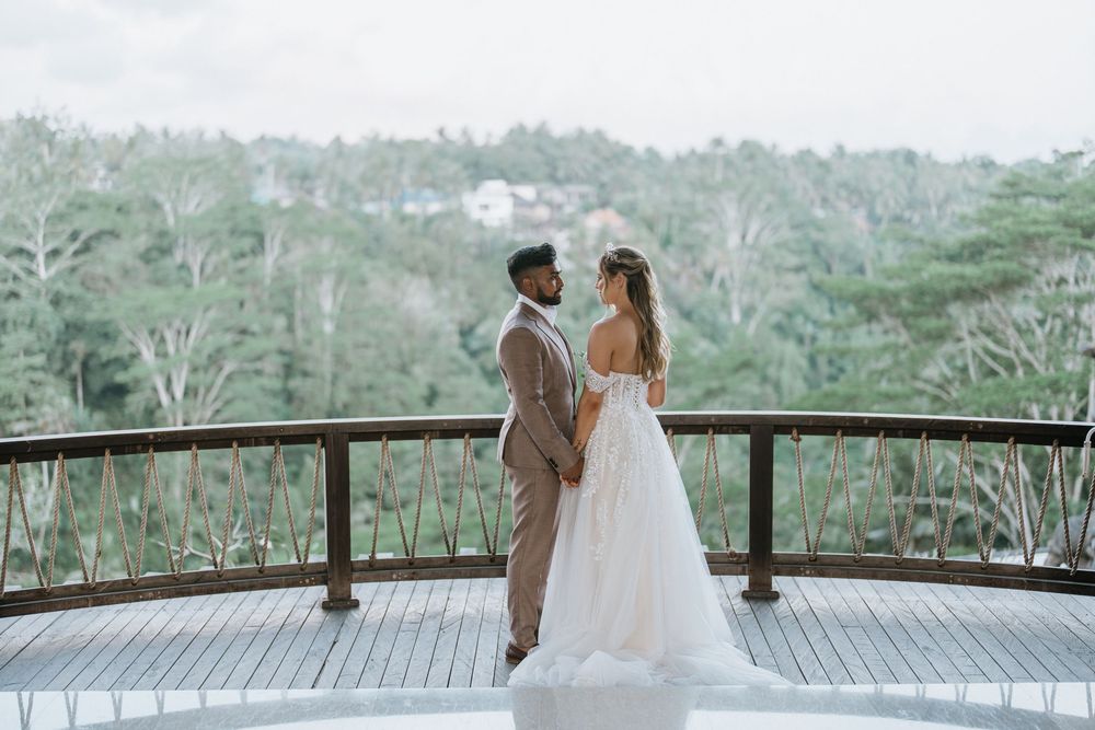 Newlyweds share intimate moment on wooden deck overlooking forest landscape.