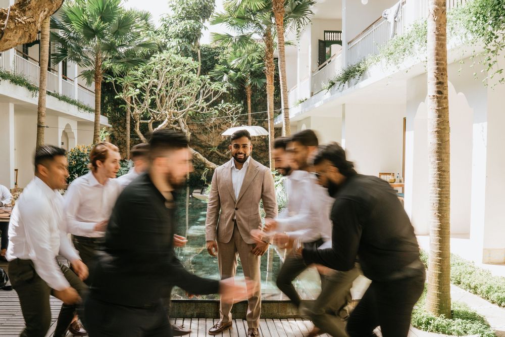 Groomsmen celebrate with playful jumping photo in tropical garden setting.