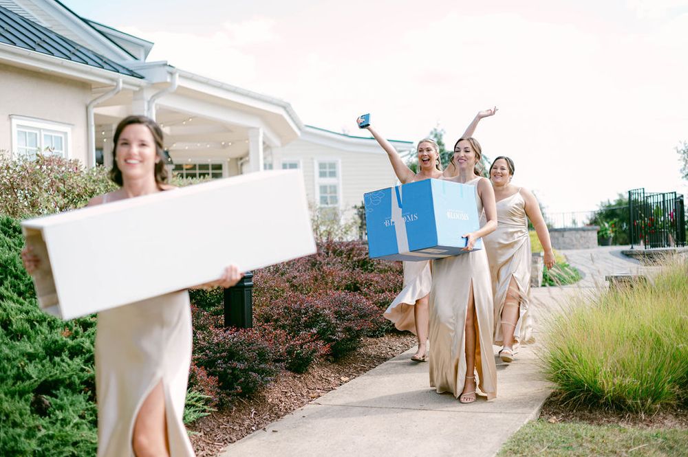 Wedding party walking down a curved pathway at a seaside venue while holding white umbrellas and parasols.