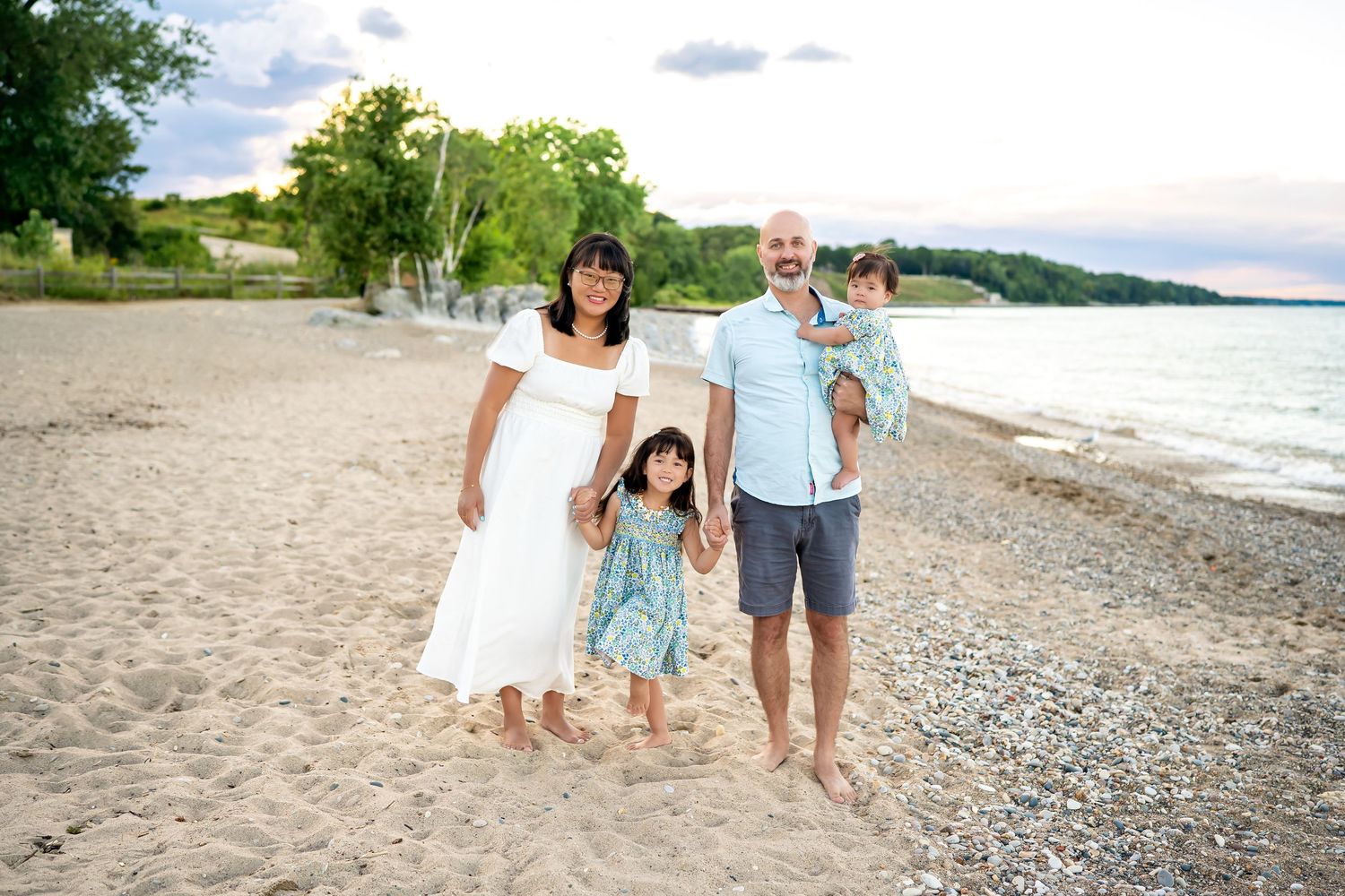 A family walks along a sandy beach in white and light blue coordinated outfits during a summer photoshoot.