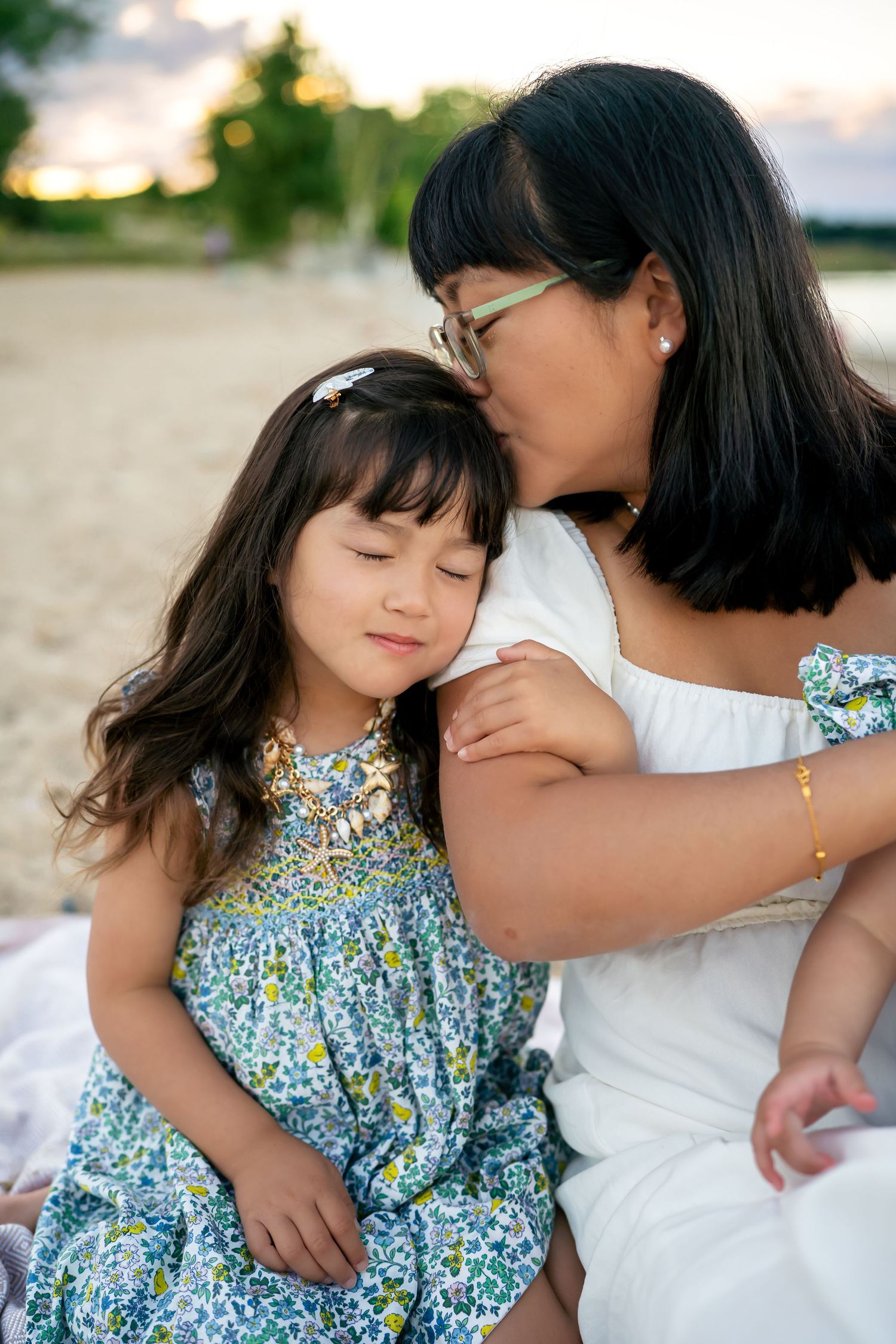 A tender moment captured between two people wearing white and floral print clothing on a beach at sunset.