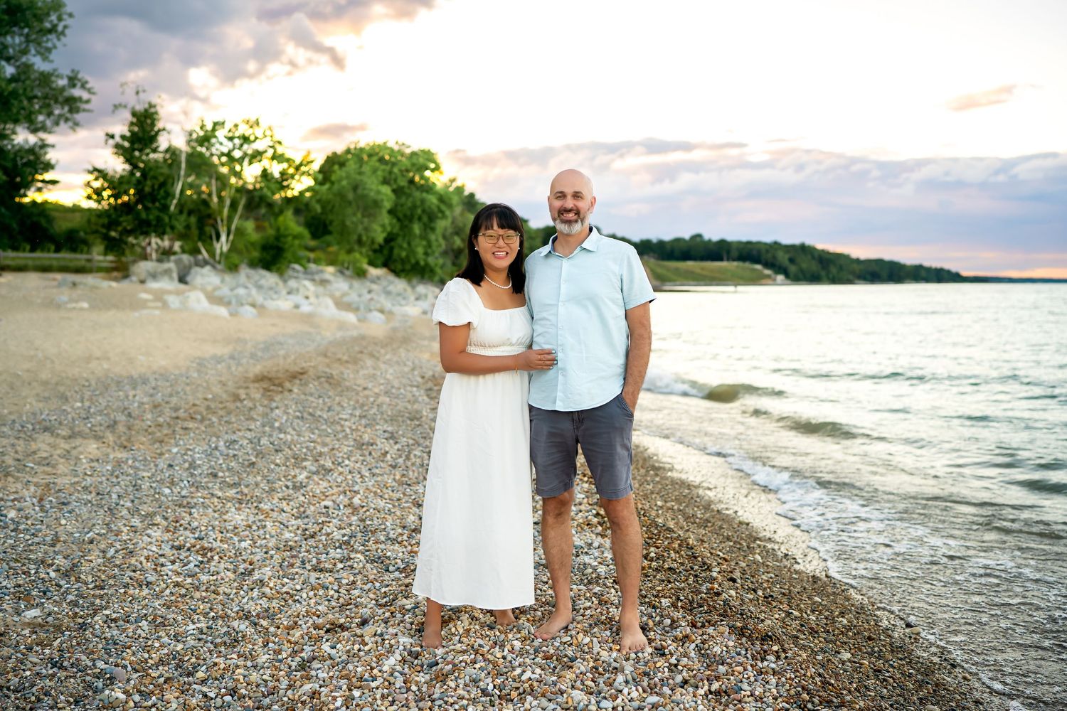 Couple enjoying a romantic evening stroll on a peaceful beach with waves and dramatic cloudy sky in the background.