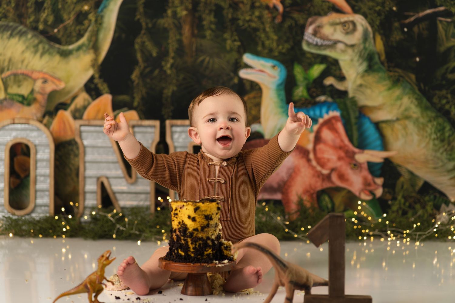Excited baby boy celebrating first birthday with dinosaur themed cake smash decoration.