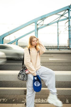 Fashion photography series on bridge with teal structural elements and passing traffic.