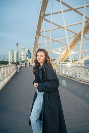Modern fashion photography on wooden bridge deck with city skyline backdrop.
