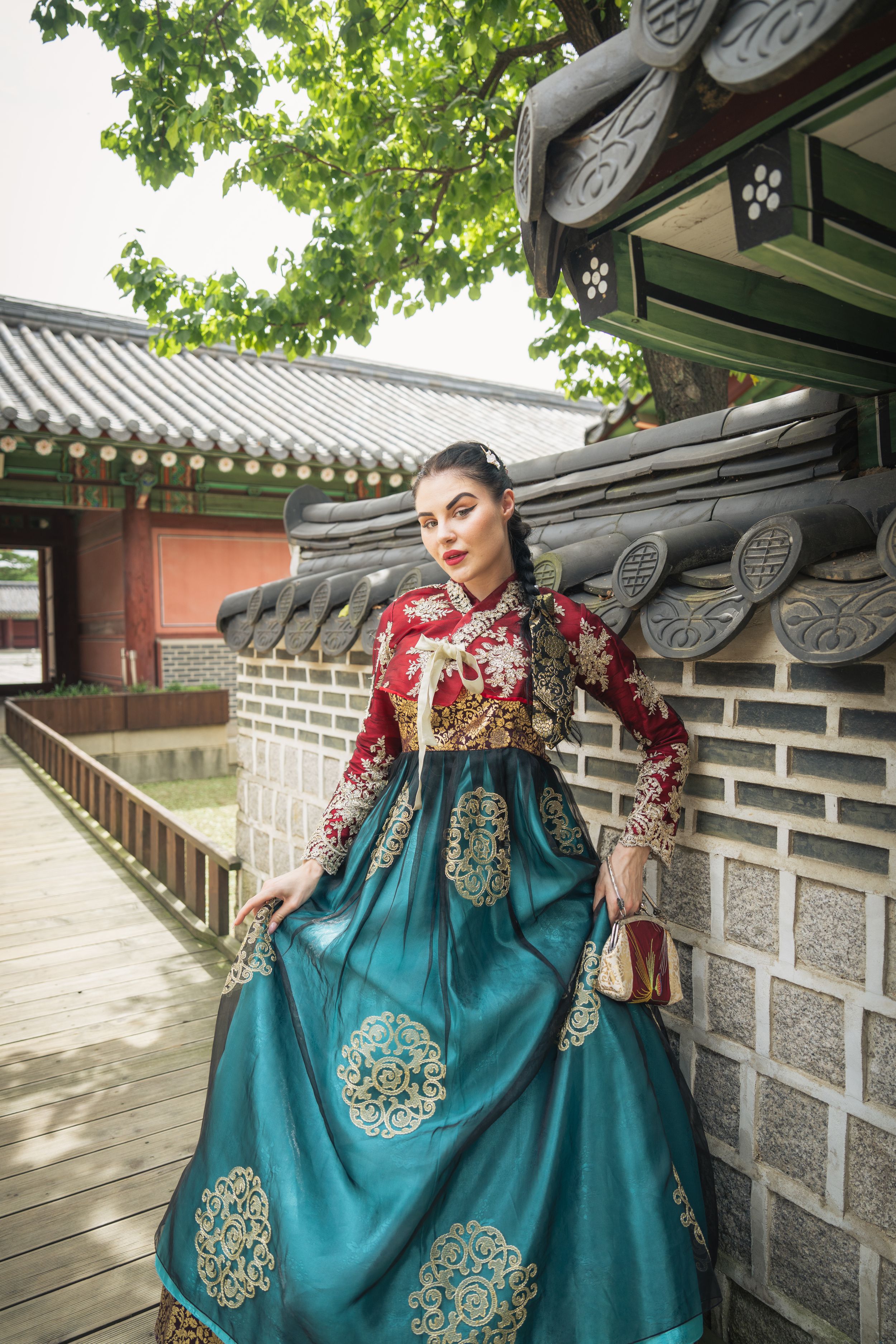Traditional Korean hanbok dress in turquoise blue with ornate gold embroidered details at a historic palace.