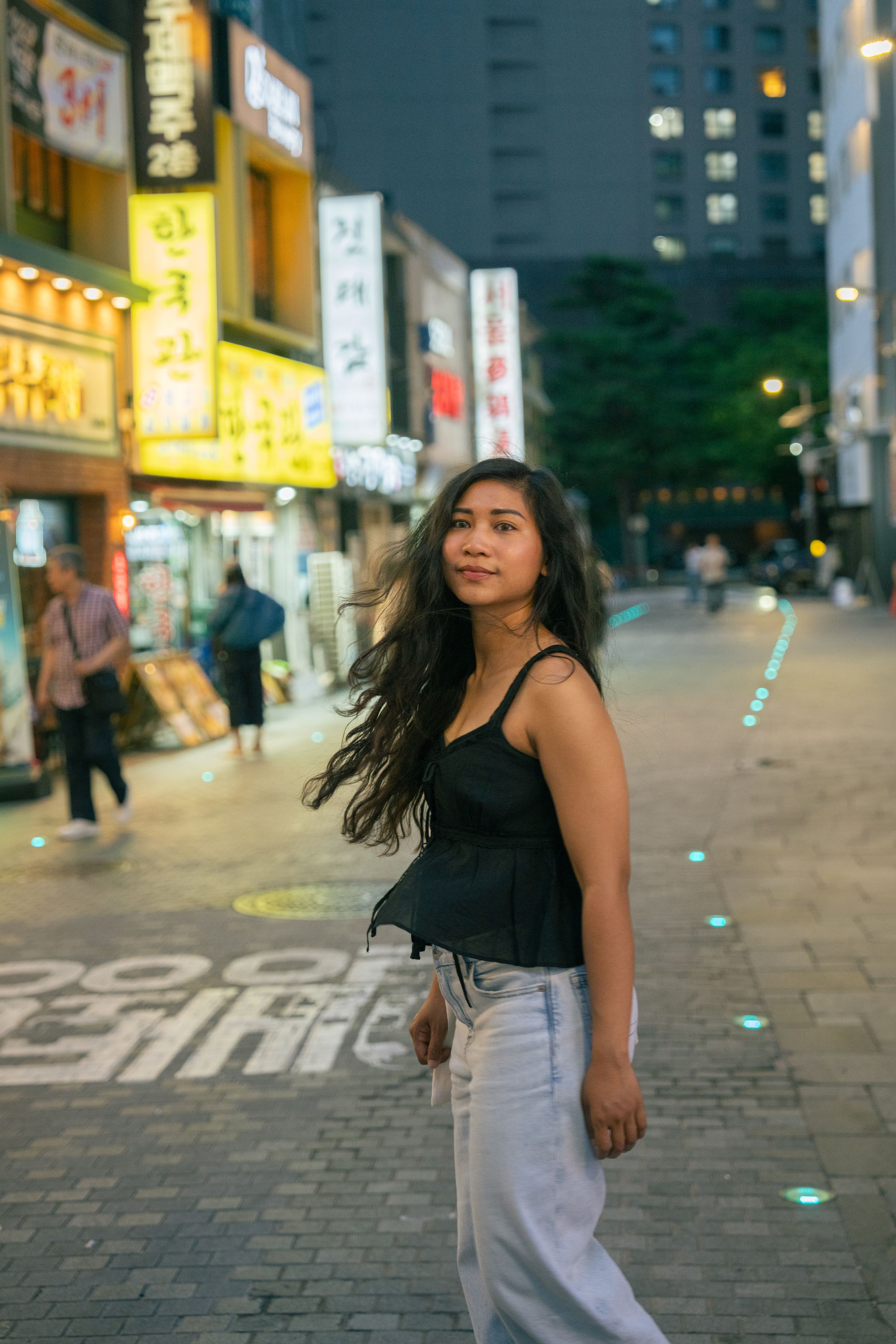 Dynamic street fashion photoshoot in an urban Asian setting with neon lights and illuminated storefronts.