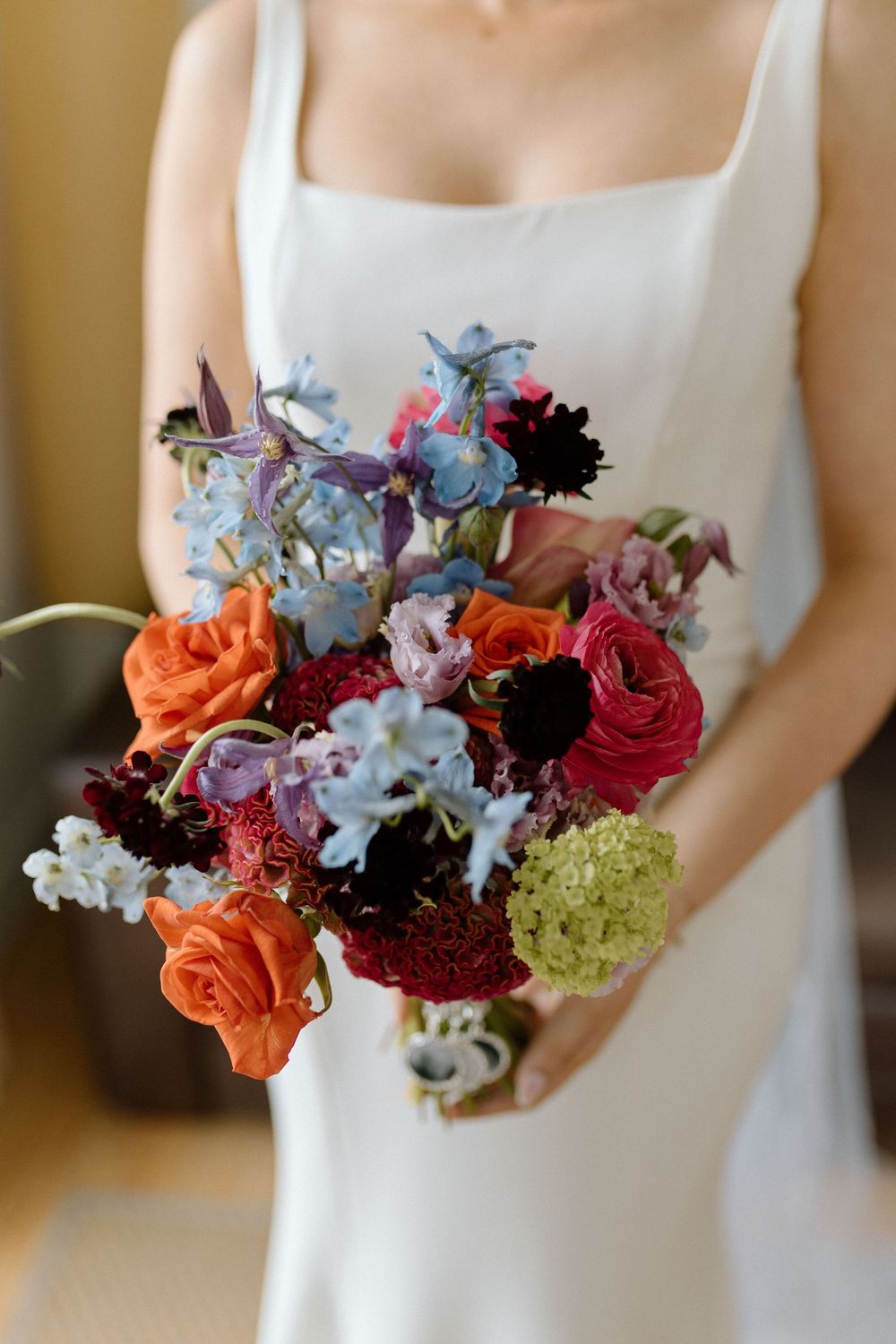A vibrant bridal bouquet featuring orange lilies, deep red dahlias, light blue delphinium and green hydrangeas.