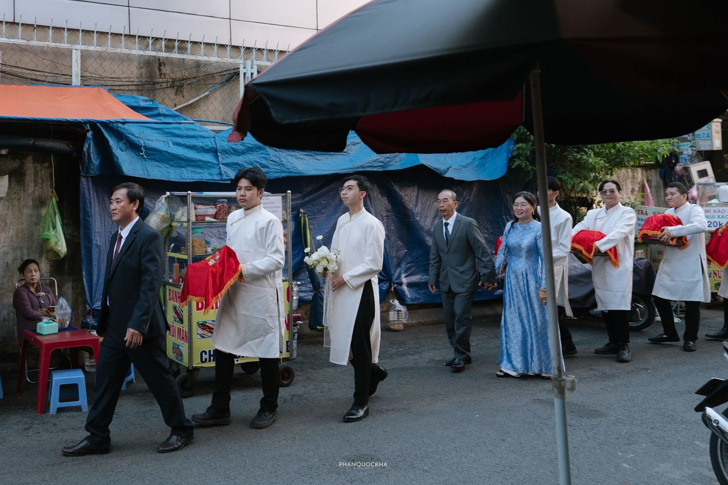 Traditional Vietnamese wedding procession moves through street with guests carrying red gift boxes.