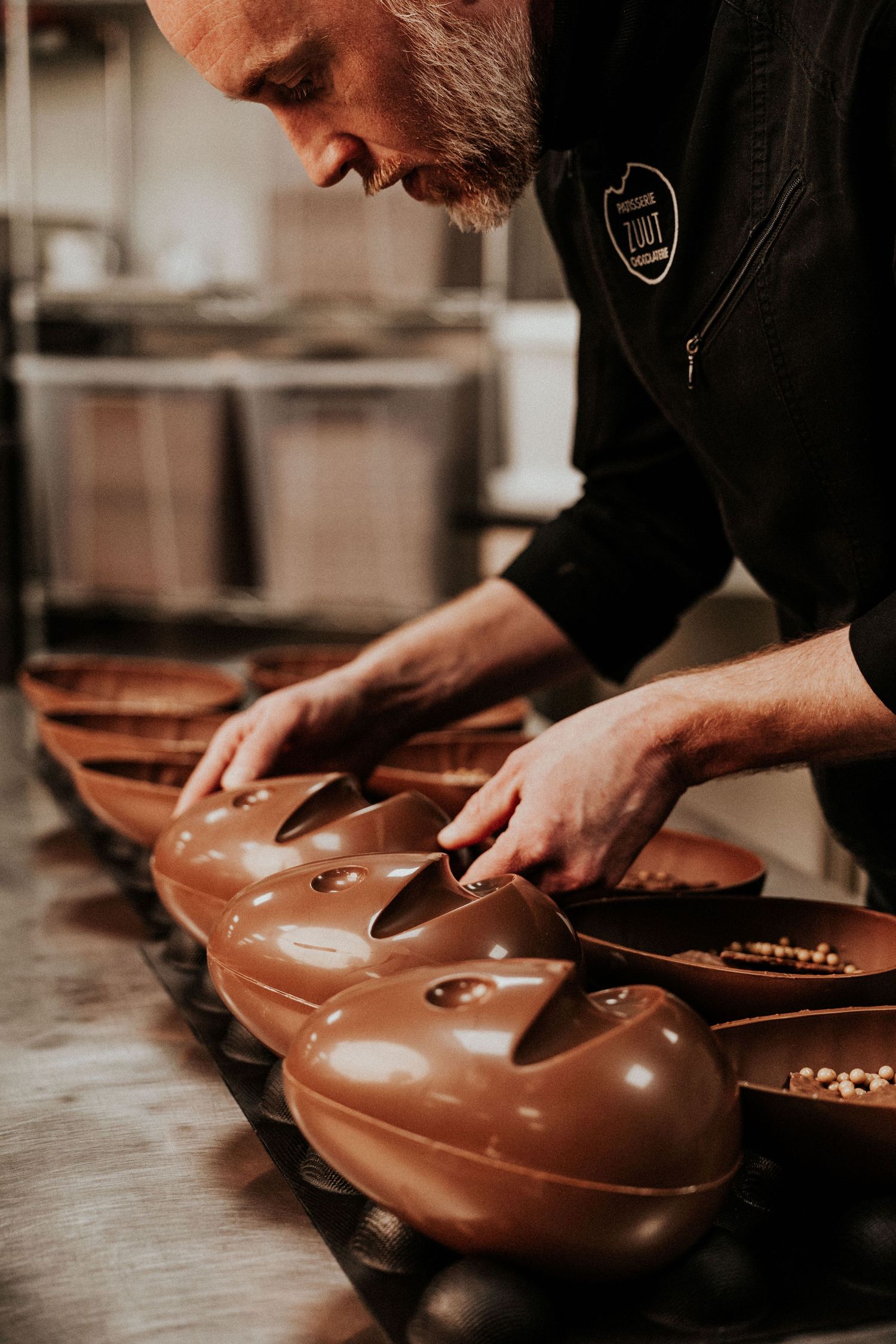 Chocolatier crafting detailed chocolate molds on wooden surface.