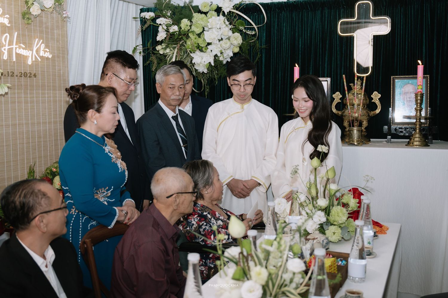 Family members gather around elders at a traditional Vietnamese ceremony with floral decorations.