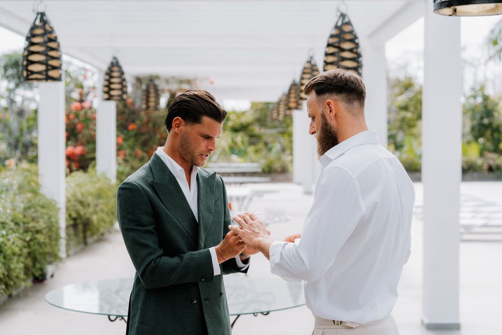 Groom and groomsman share an emotional exchange during a wedding ceremony under decorative pagoda lanterns at an outdoor venue.
