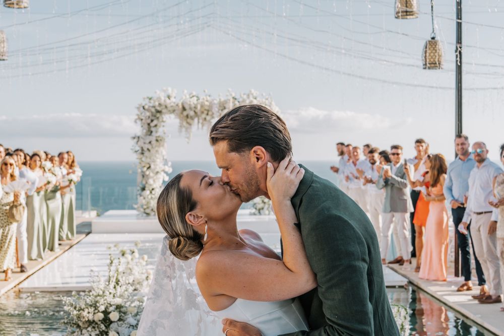 A romantic seaside wedding moment with a couple kissing and embracing at a beach ceremony.