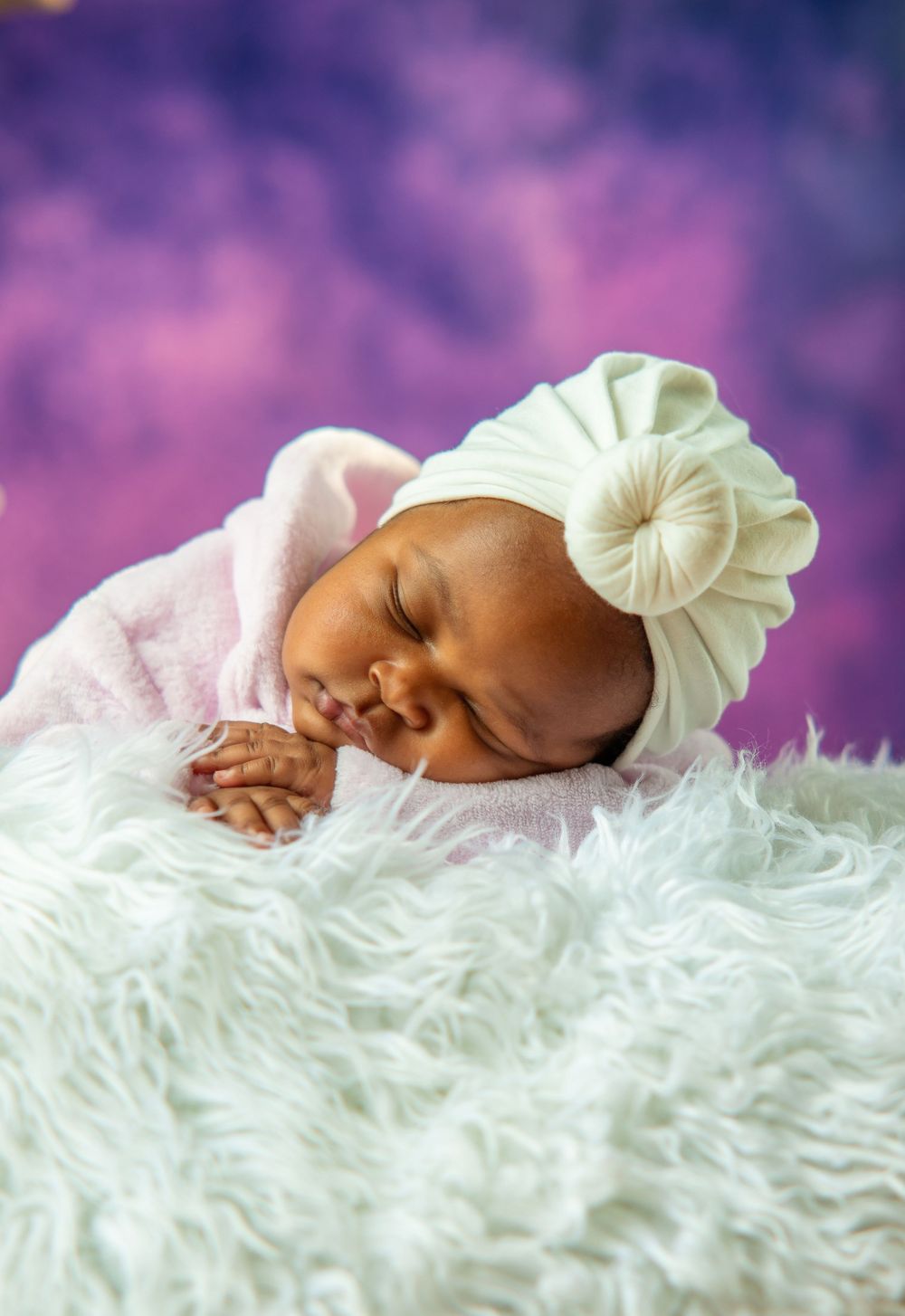 Peaceful newborn photography on soft white fur against purple backdrop.