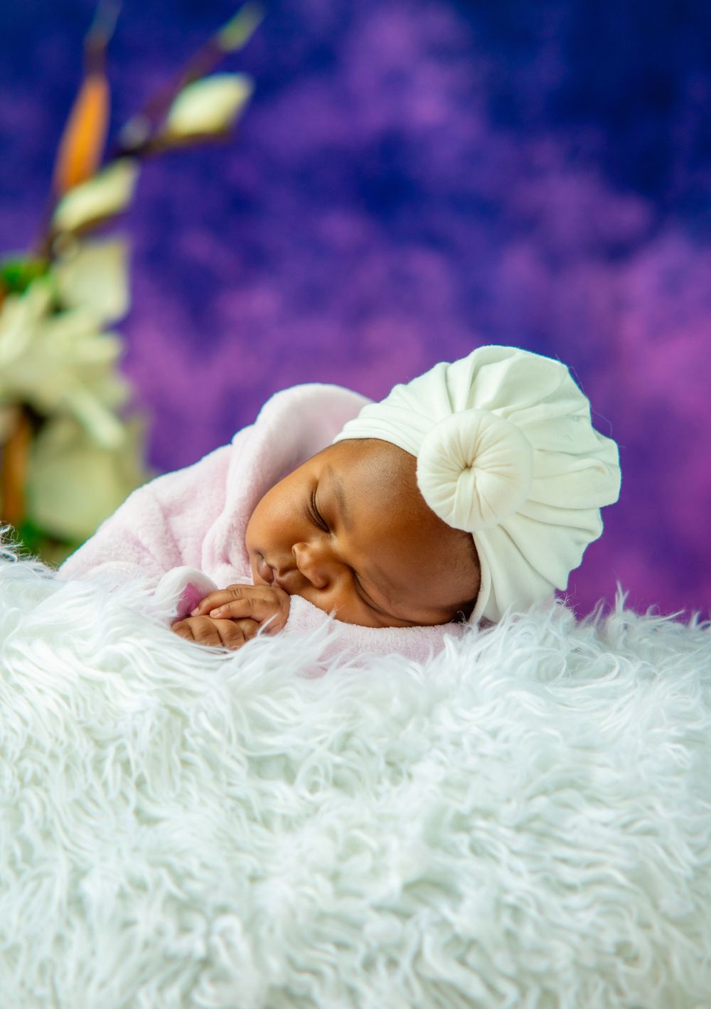 Sleeping infant wrapped in white fabric against purple backdrop.