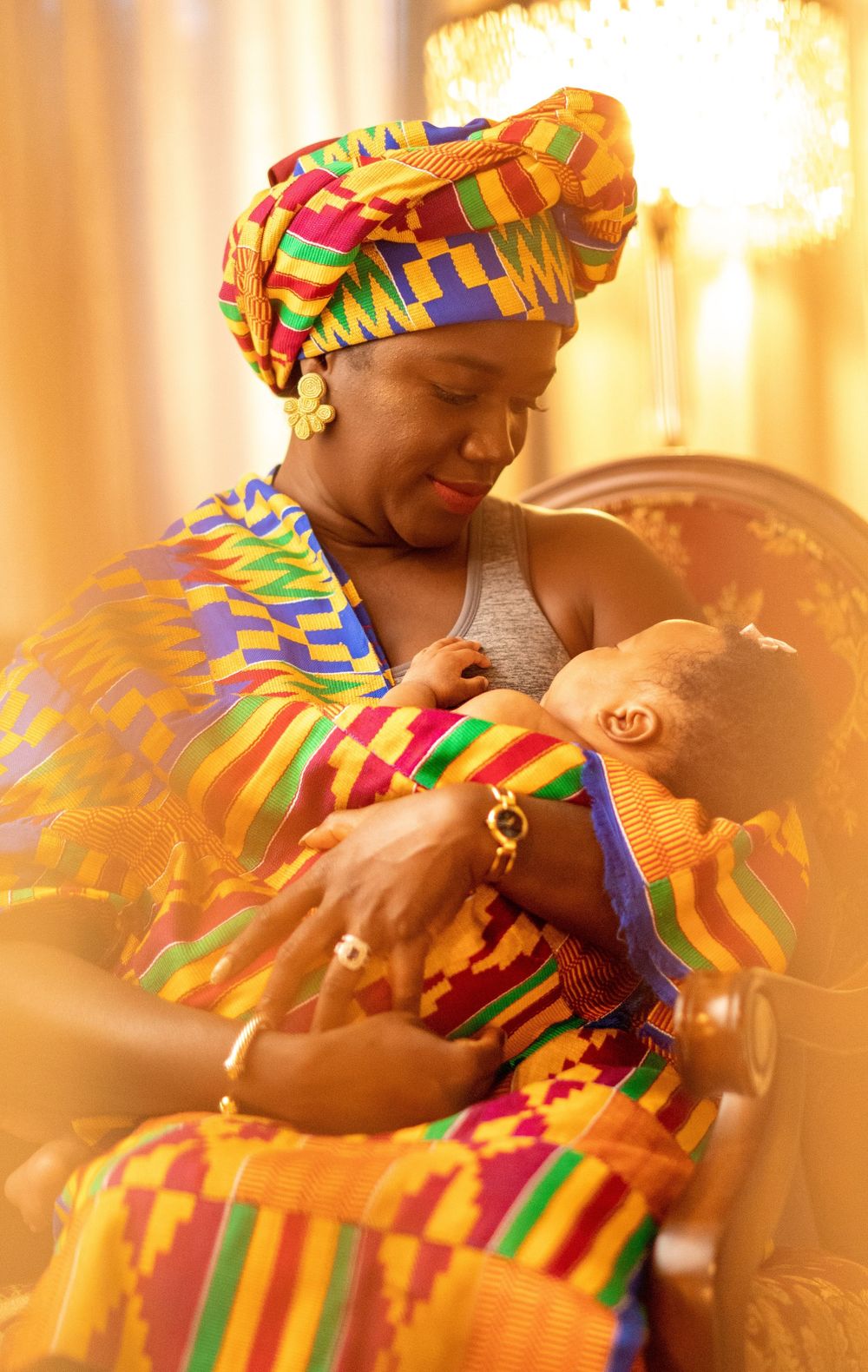 Intimate motherhood moment captured in warm tones with traditional African kente print attire.