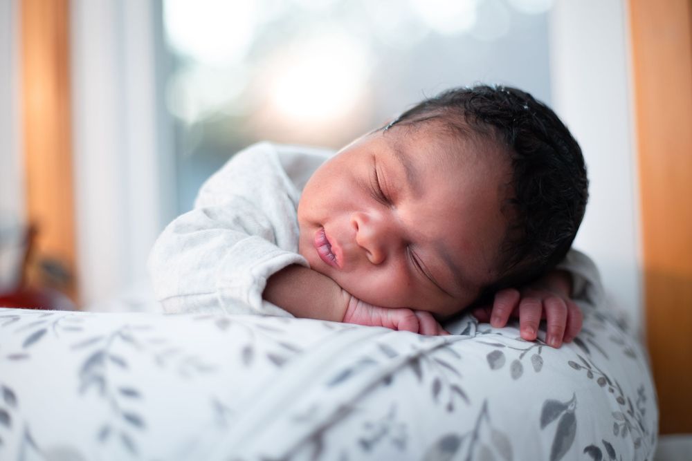Sleeping newborn on floral patterned bedding in natural light.