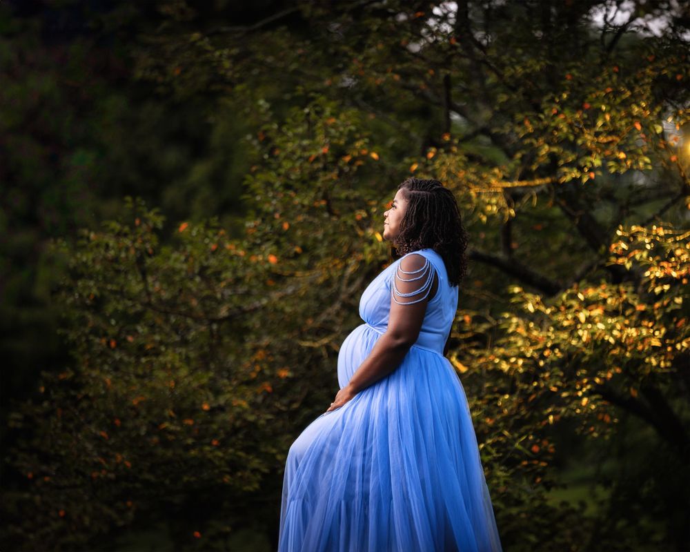 Ethereal maternity portraits with blue gown against autumn foliage background.