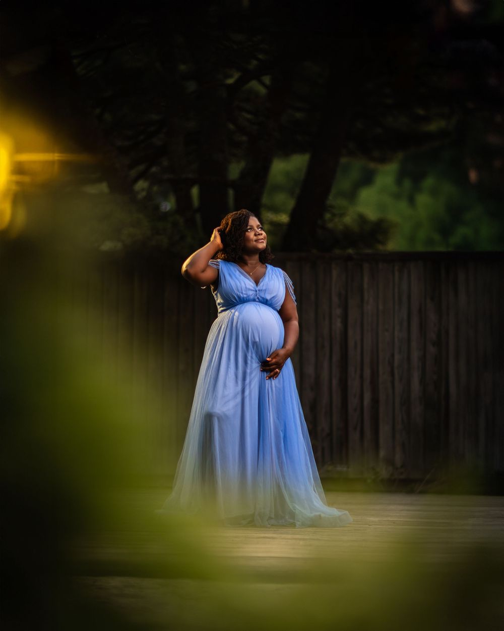 Romantic maternity photos in flowing blue dress captured in garden setting.