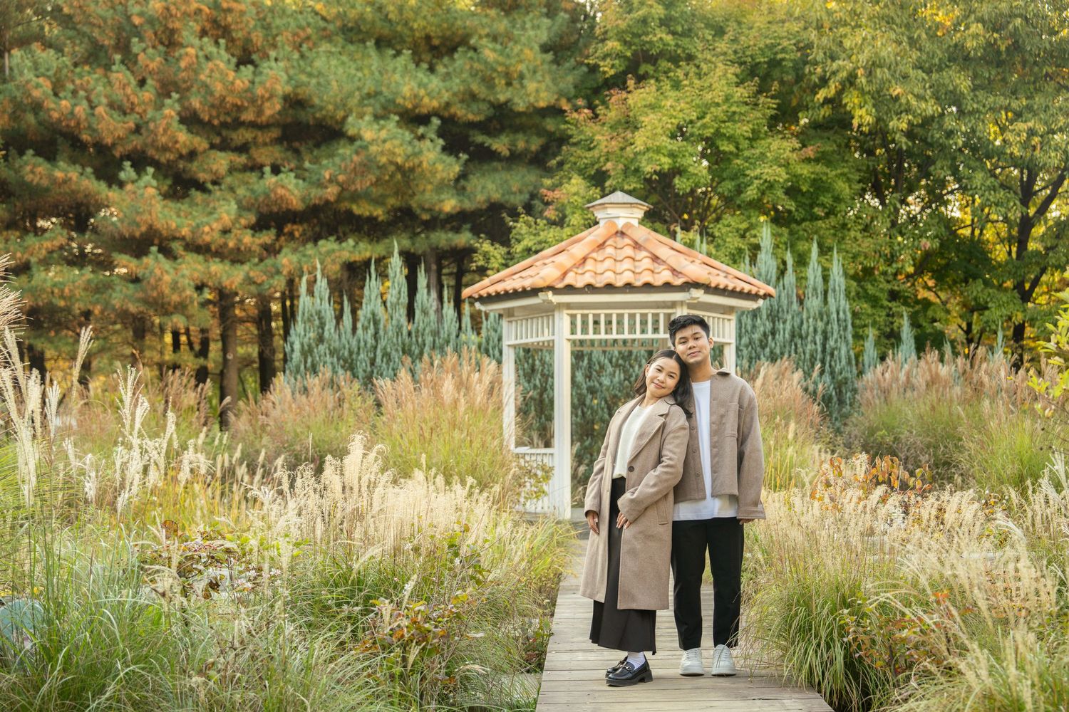 A couple embraces in a romantic garden setting with a white gazebo and lush greenery in the background.