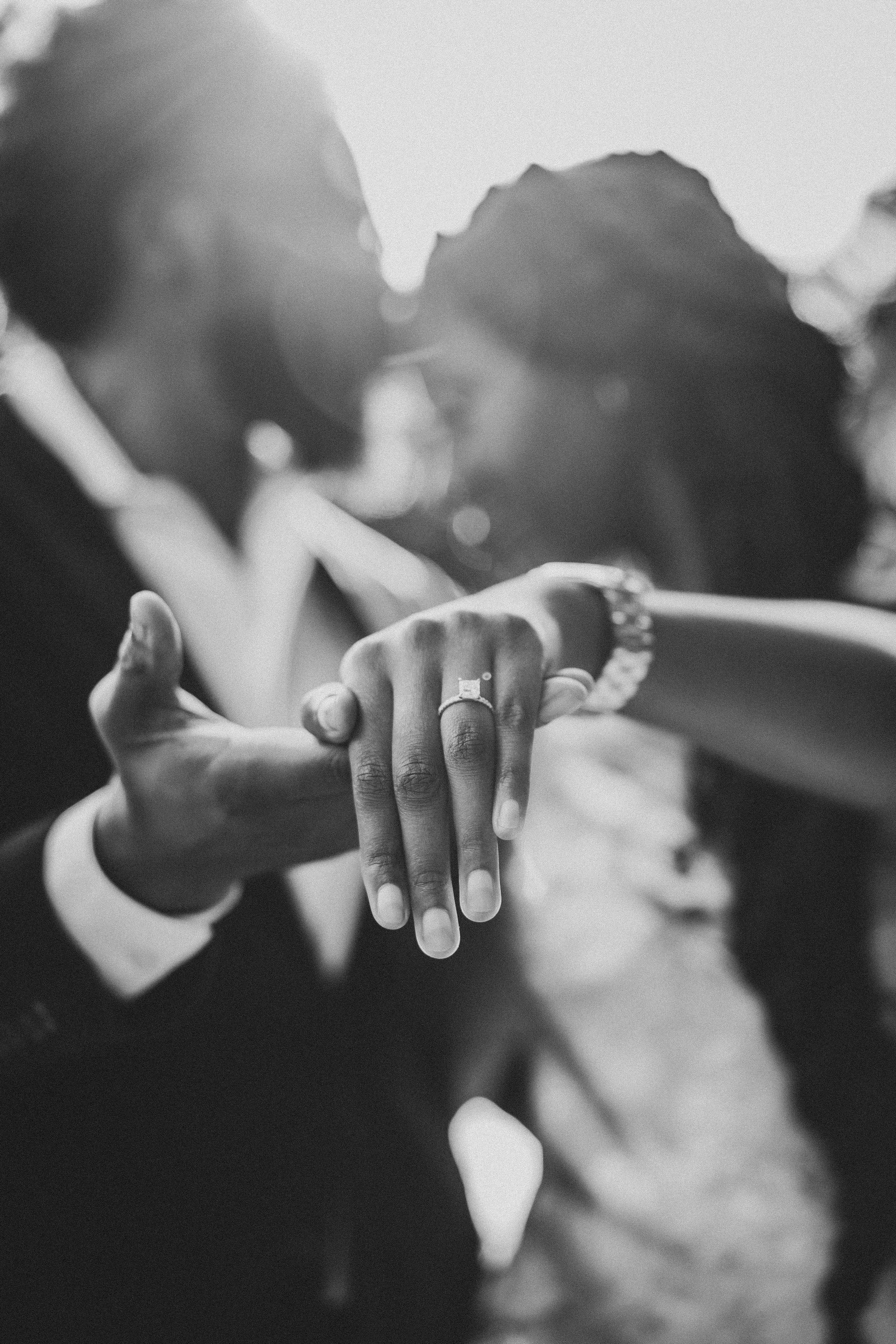 Close-up black and white photo of two hands reaching towards each other with rings in a romantic gesture.