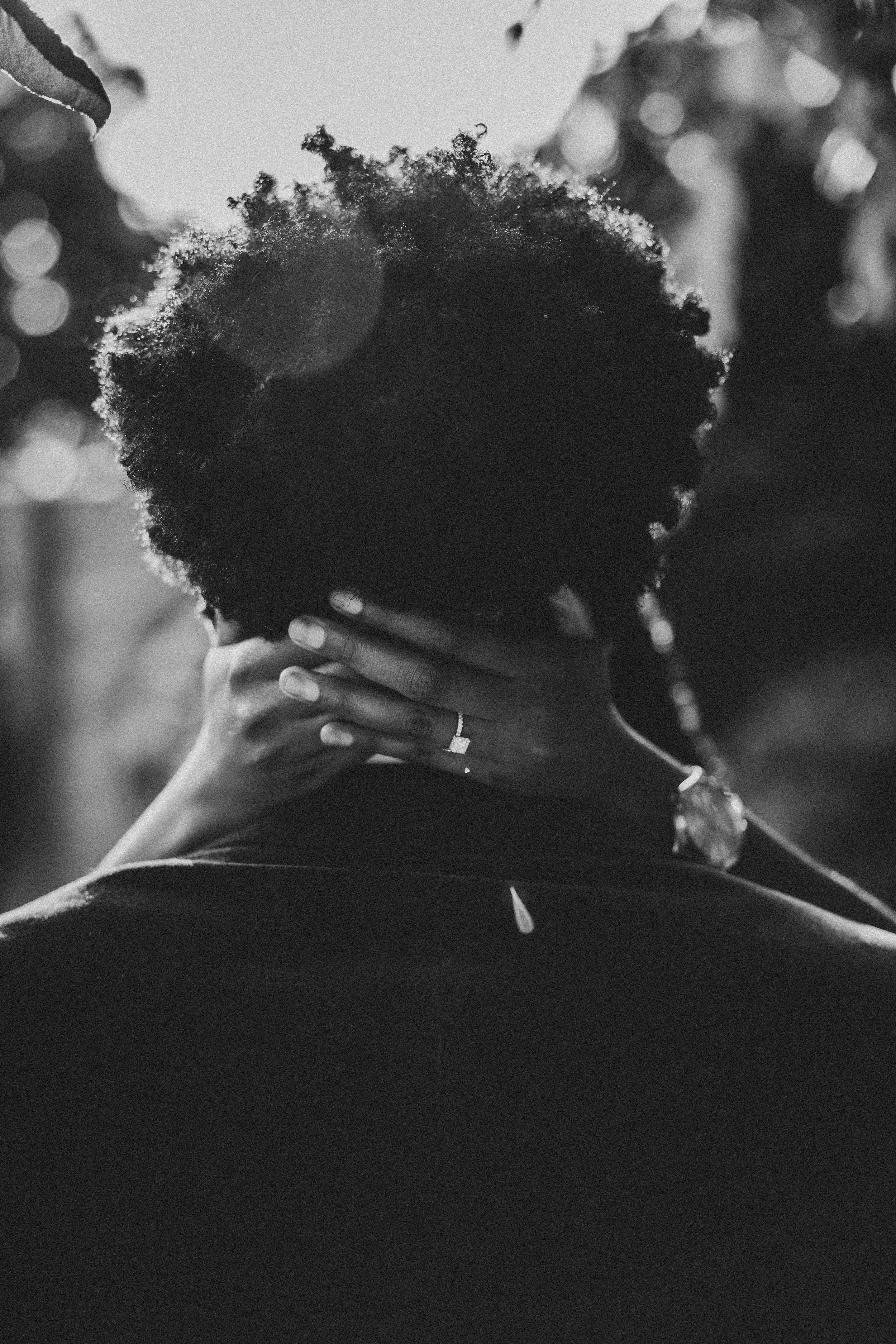 Black and white silhouette of curly hair against a soft bokeh background displaying the engagement ring