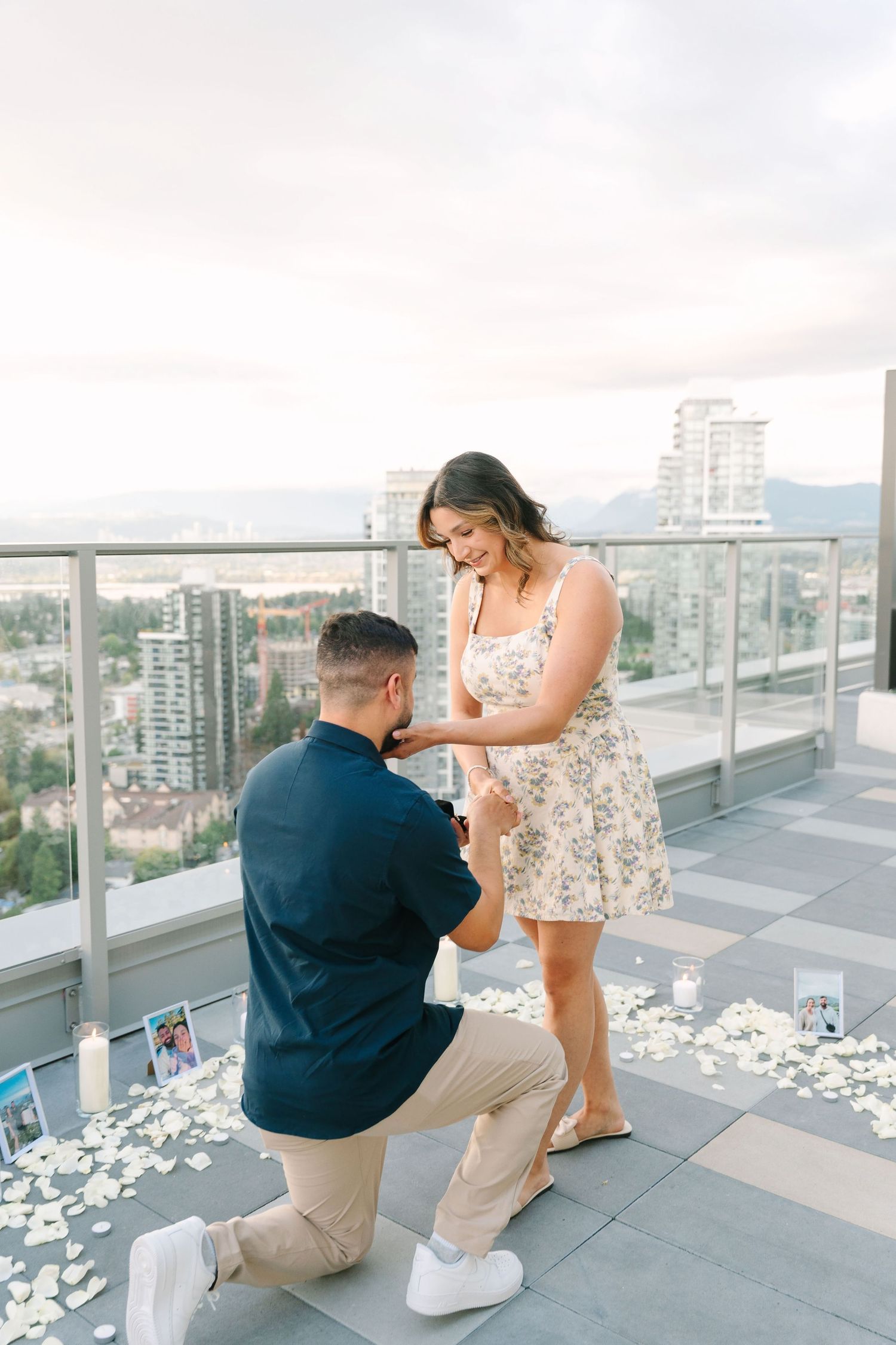 A proposal moment captured on an outdoor balcony surrounded by rose petals and candles.
