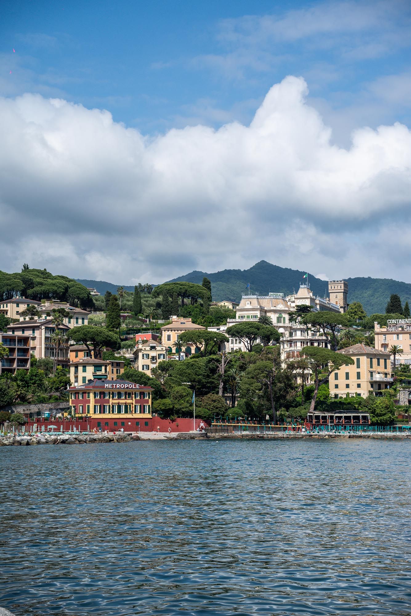 Colorful hillside buildings and villas overlook the blue waters of the Italian Riviera on a sunny summer day.