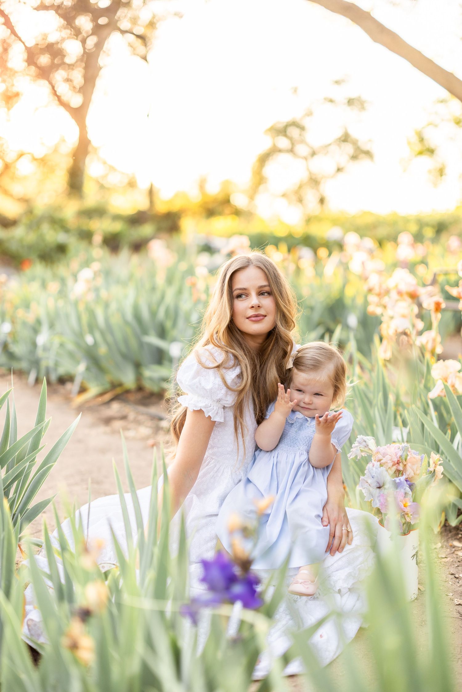 Mother and child sitting among blooming iris flowers in a garden at golden hour.