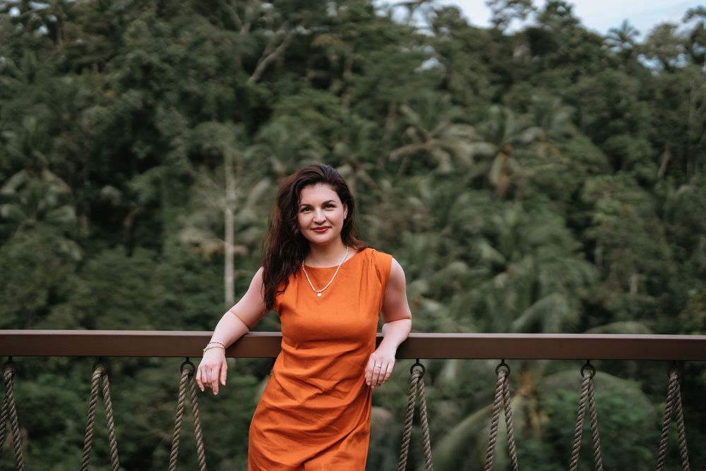 Someone wearing an orange dress stands on a wooden deck overlooking a tropical forest landscape.