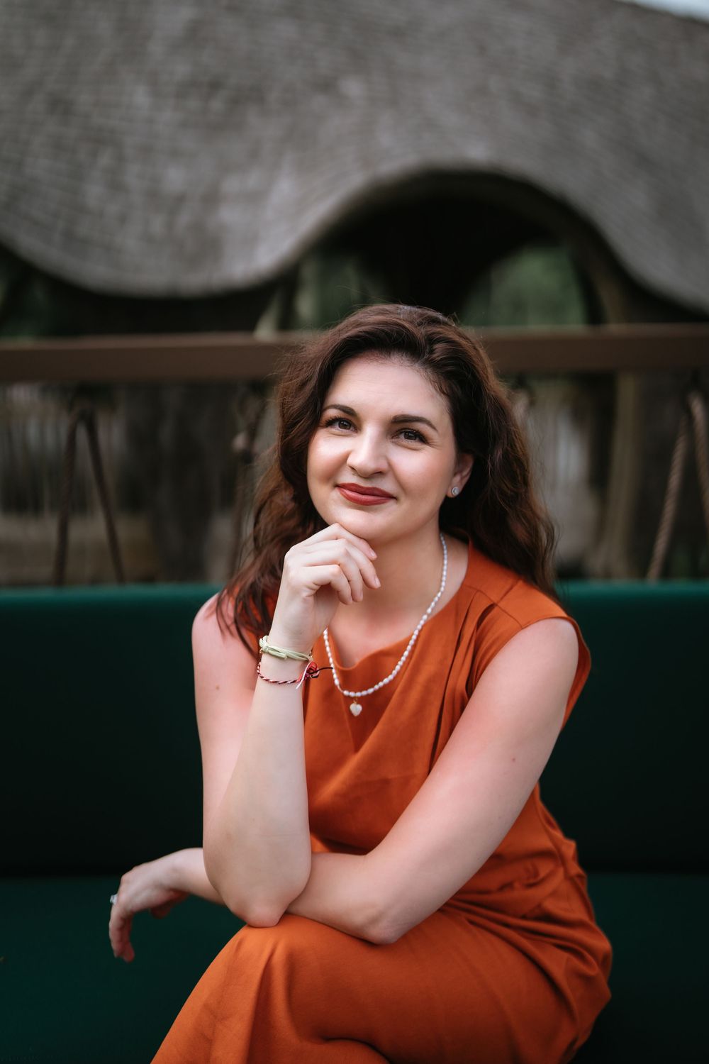 A relaxed pose on dark furniture against a thatched roof background.
