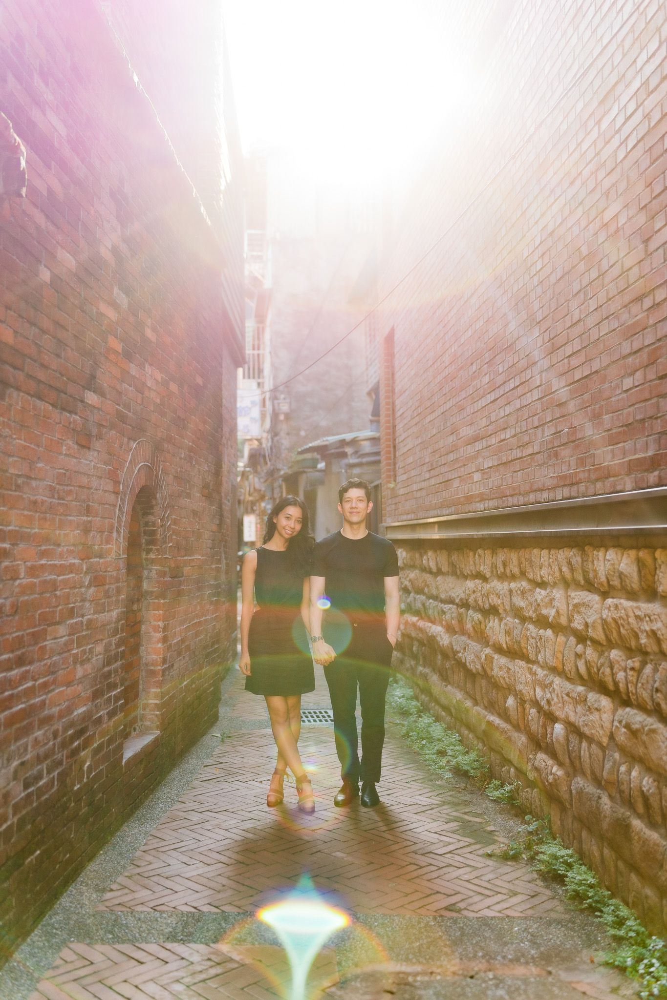 Two people stand in a narrow brick alley with dramatic lighting and shadows creating an atmospheric scene.