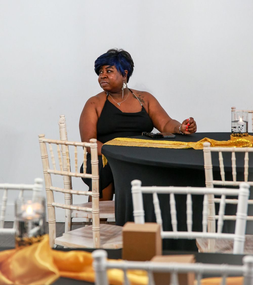 A person in a black top sits at a formal dining table with white chiavari chairs and yellow table decor.
