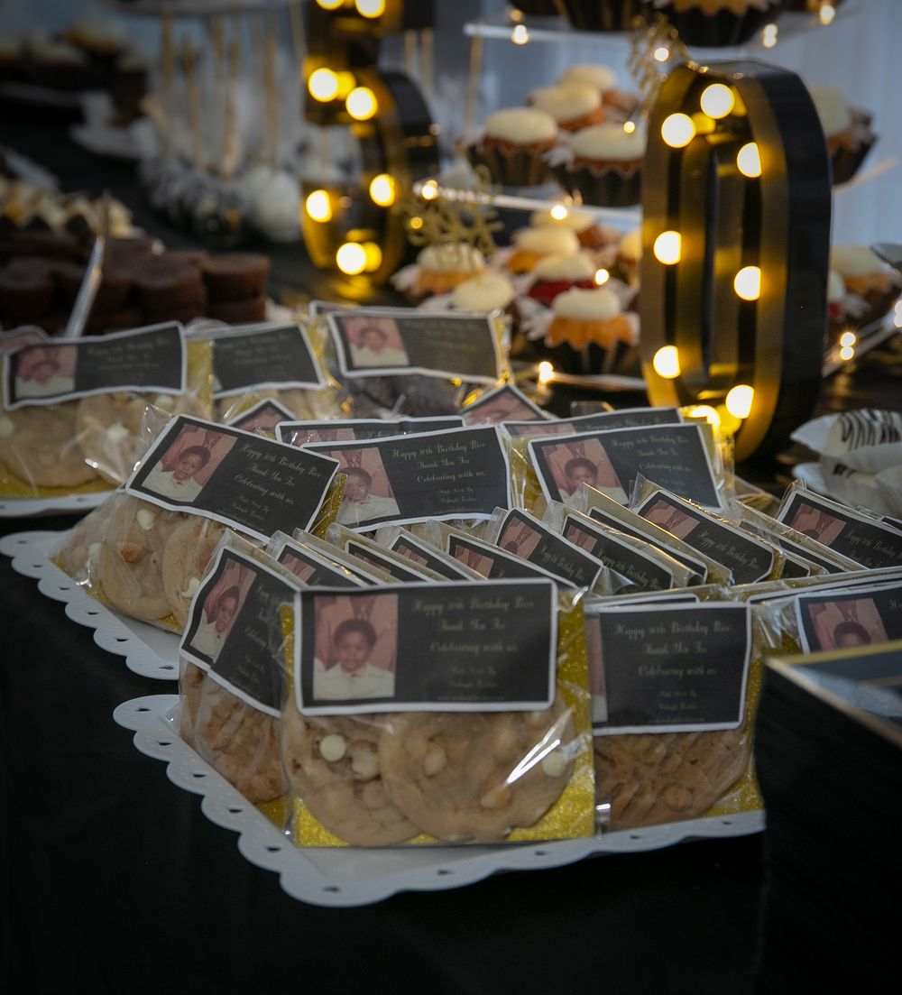 Packaged cookies with photo labels arranged on white doilies with decorative lighting in the background.