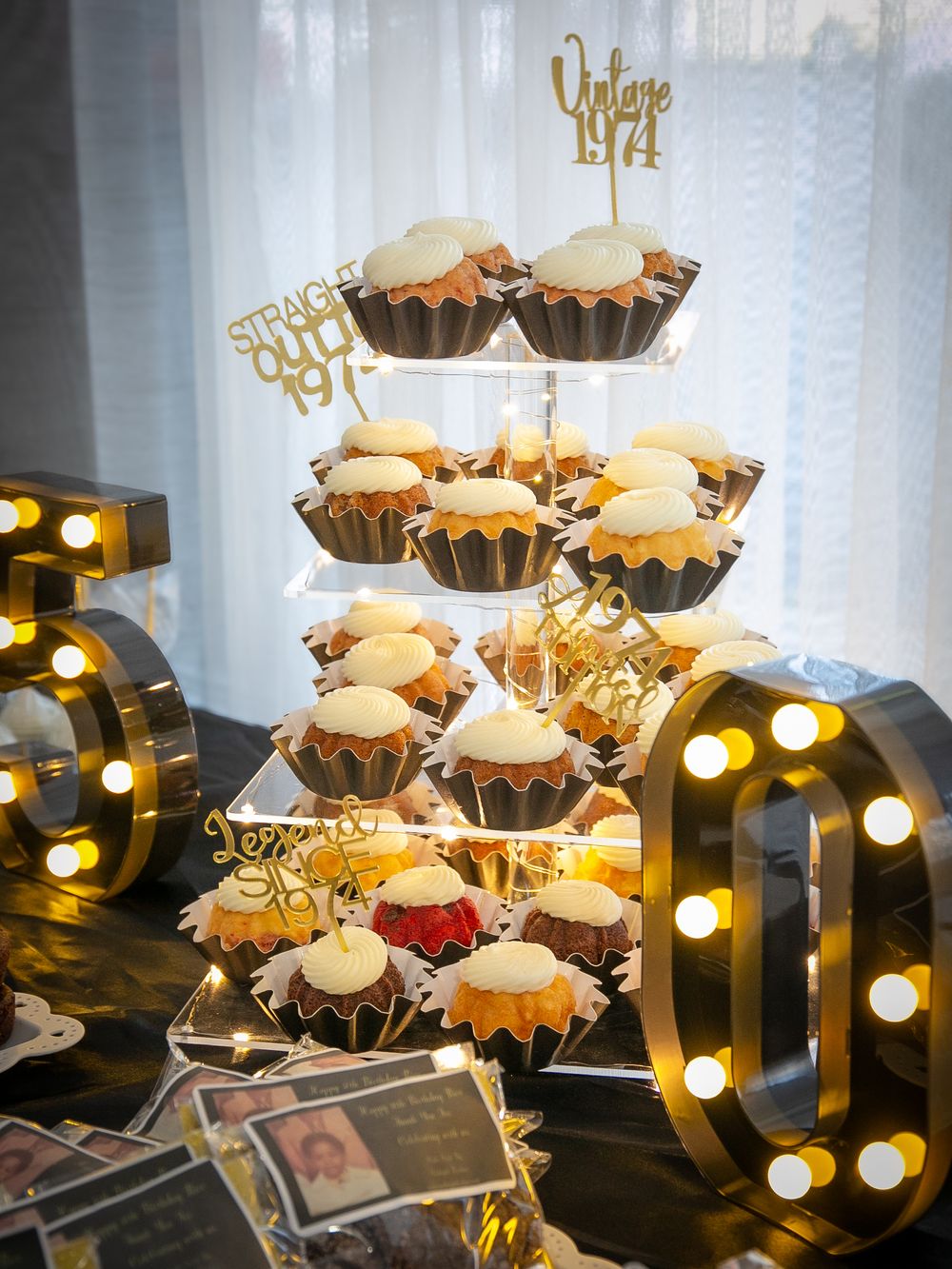 Tiered cupcake display with gold decorations and glowing marquee letters creates an elegant party atmosphere.