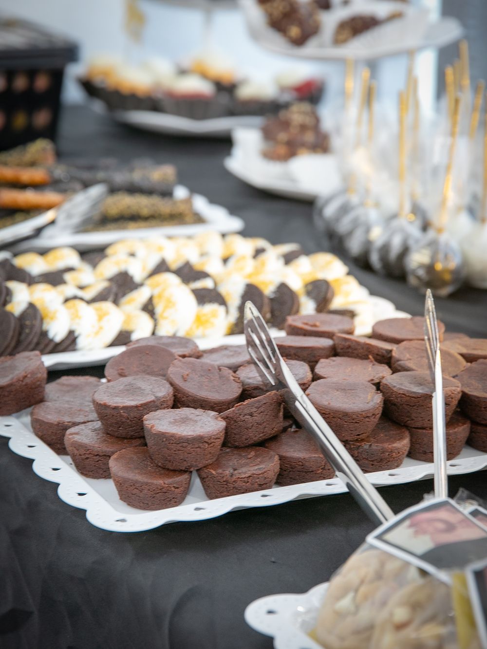 Close-up view of chocolate dessert bites and cookies arranged on white serving platters at a dessert buffet table.