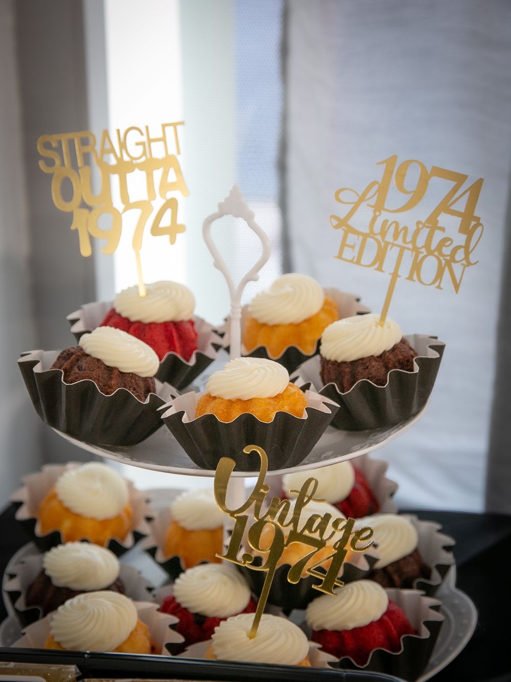 Cupcakes decorated with gold toppers reading "1974 Limited Edition" and "Straight Outta 74" displayed on tiered stand.