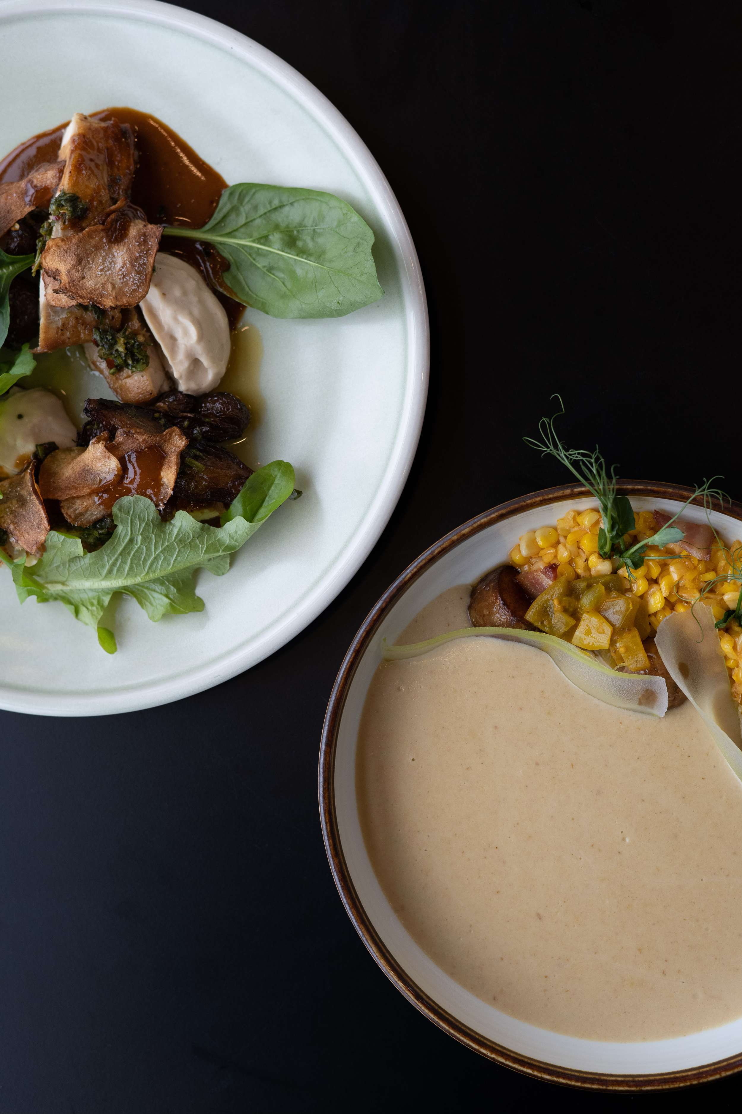 Elegant plating of chicken with corn and creamy sauce on white dinnerware against dark background.