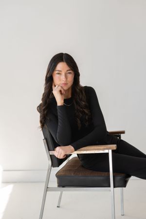 Relaxed portrait session on modern chair showing casual professional style in black.