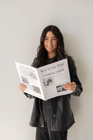 Professional photo series showing someone in a black jacket reading a real estate newspaper against a white wall.